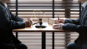 Two lawyers in suits discussing legal matters at a desk with a gavel, scales of justice, and a law book, symbolizing law and justice